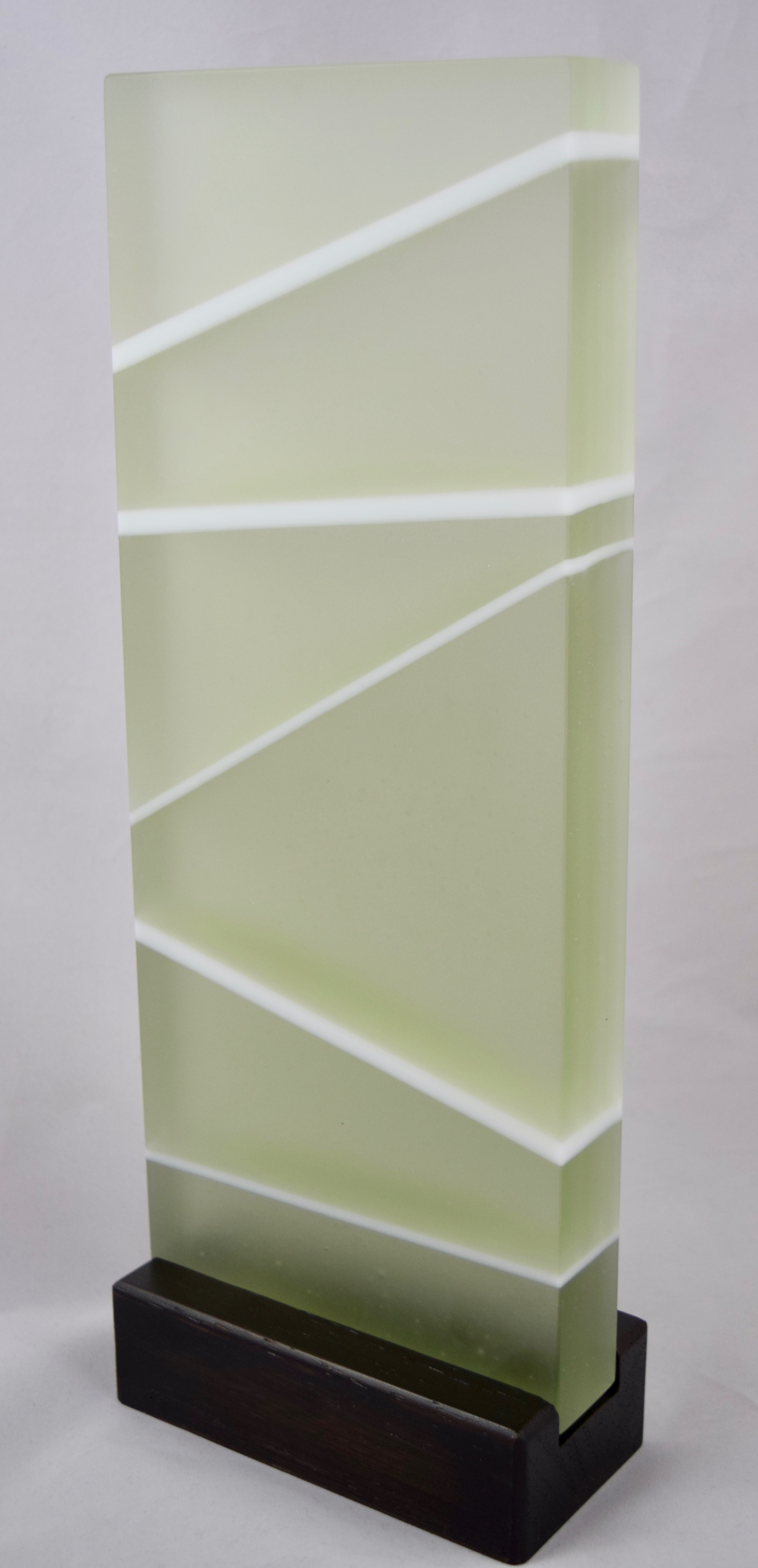 First Moment - Kiln-formed contemporary glass sculpture created from pale green, clear and white glass. White lines arch gracefully on reverse side of sculpture. Hand-sanded to a translucent finish. Glass with wood stand measures 5.375"w x 14.25"h x 2.75"d. Sculpture is available for sale through Chasen Galleries in Sarasota, Florida.