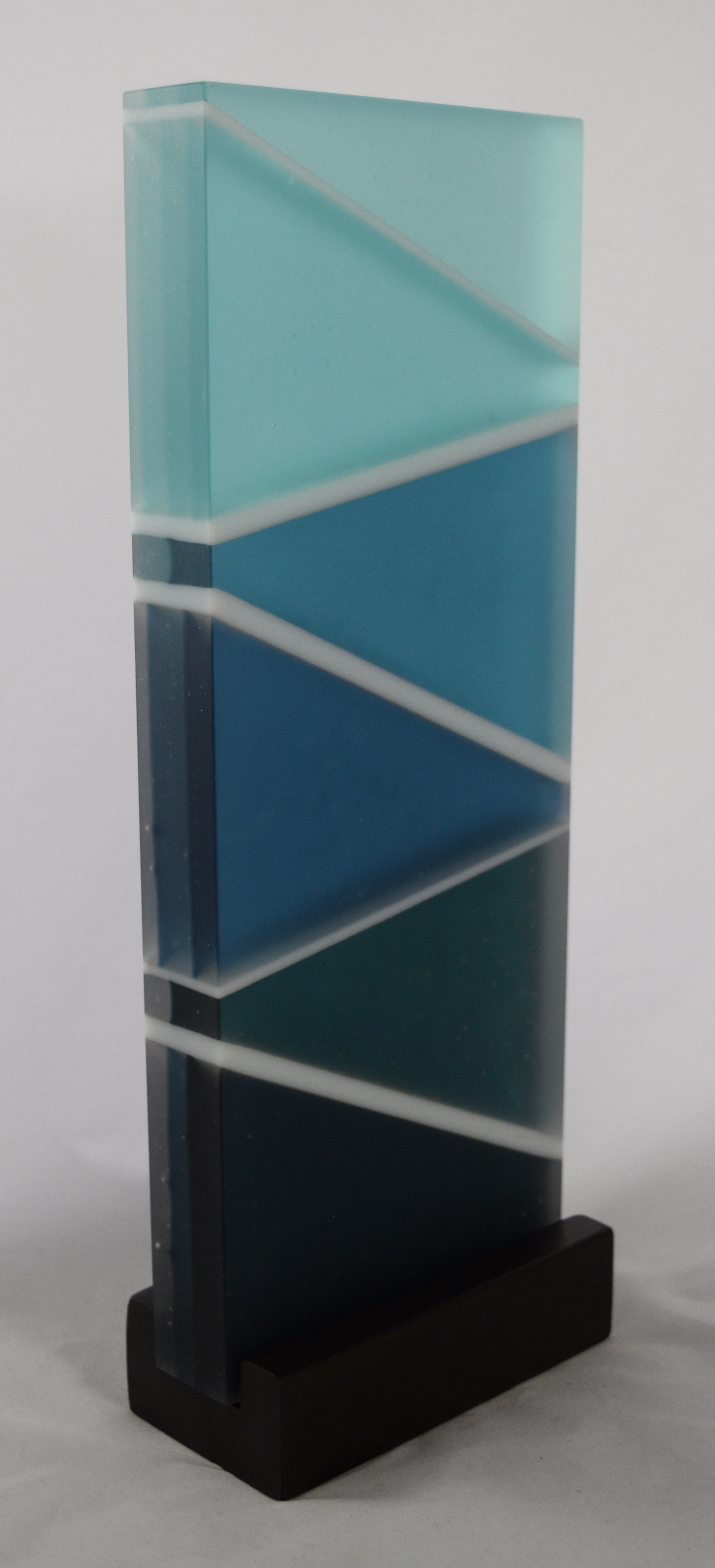 Rhythm of the Water - Kiln-formed glass sculpture created from various shades of blue and white glass. Lit best by natural light from the back. Hand-sanded to a translucent finish. Glass with wood stand measures 14.5 x 5.5 x 2.75". Available for purchase through Chasen Galleries in Richmond, Virginia.
