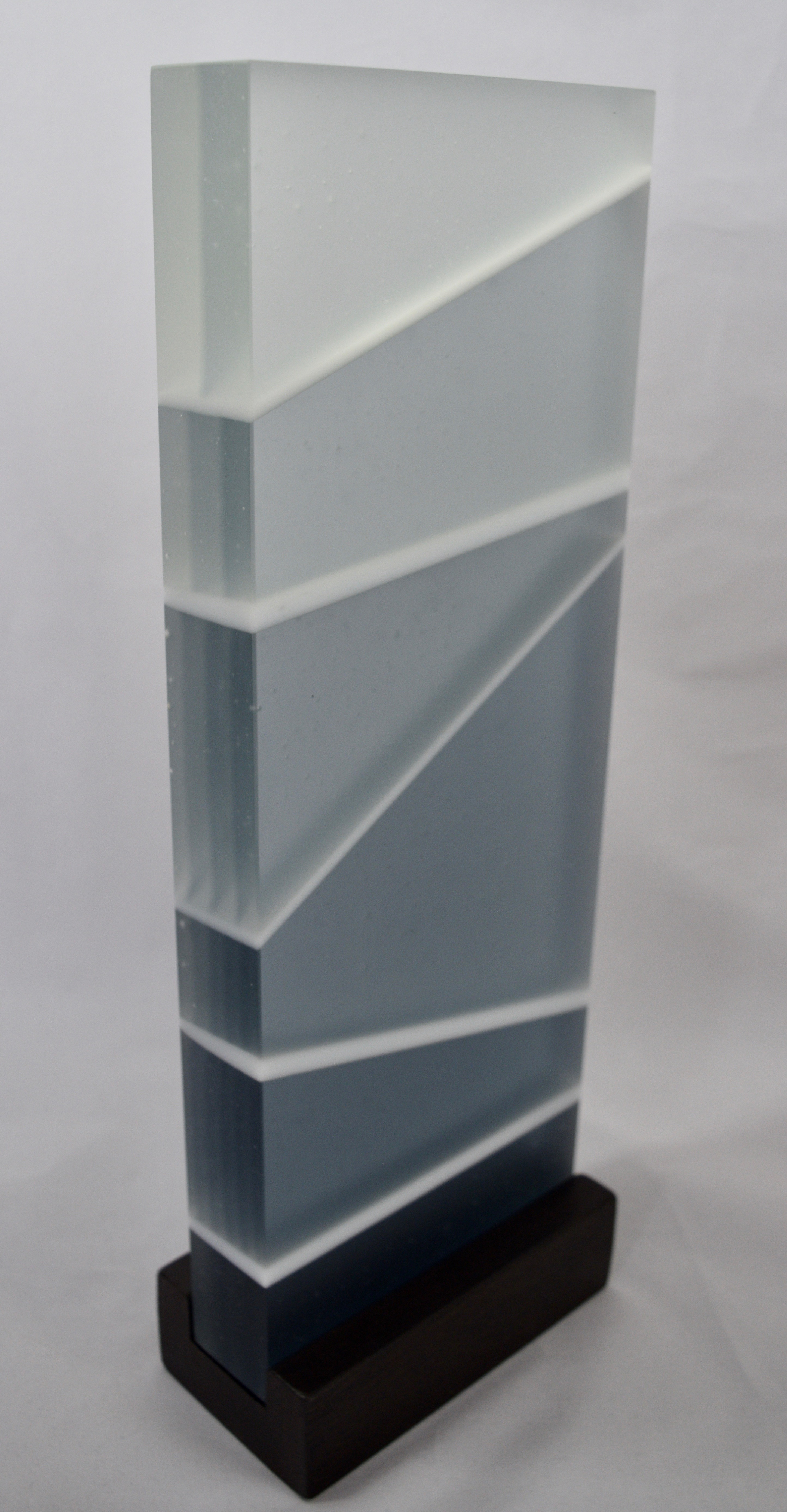 Twilight - Kiln-formed glass sculpture created from various shades of blue and white glass. Hand-sanded to a translucent finish. Glass with wood stand measures 14.125 x 5.125 x 2.75". Available for purchase.